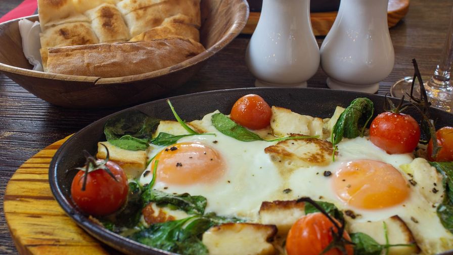 Huevos cocinados con espinacas y tomates en plato oscuro.