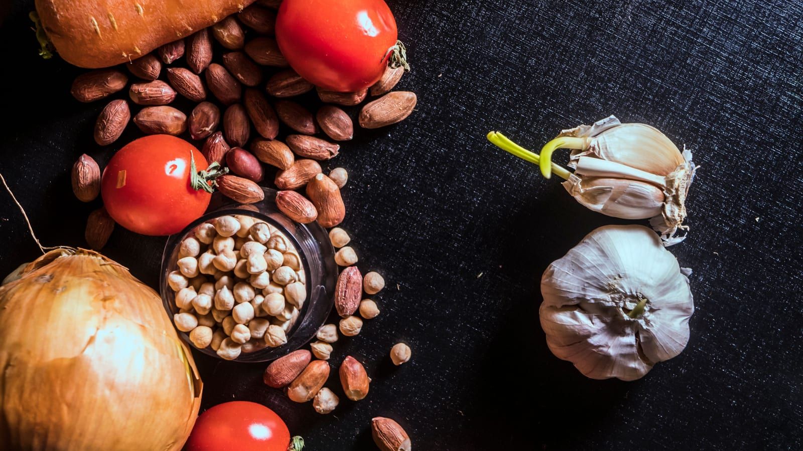 Verduras frescas, frutos secos y especias sobre una superficie oscura.